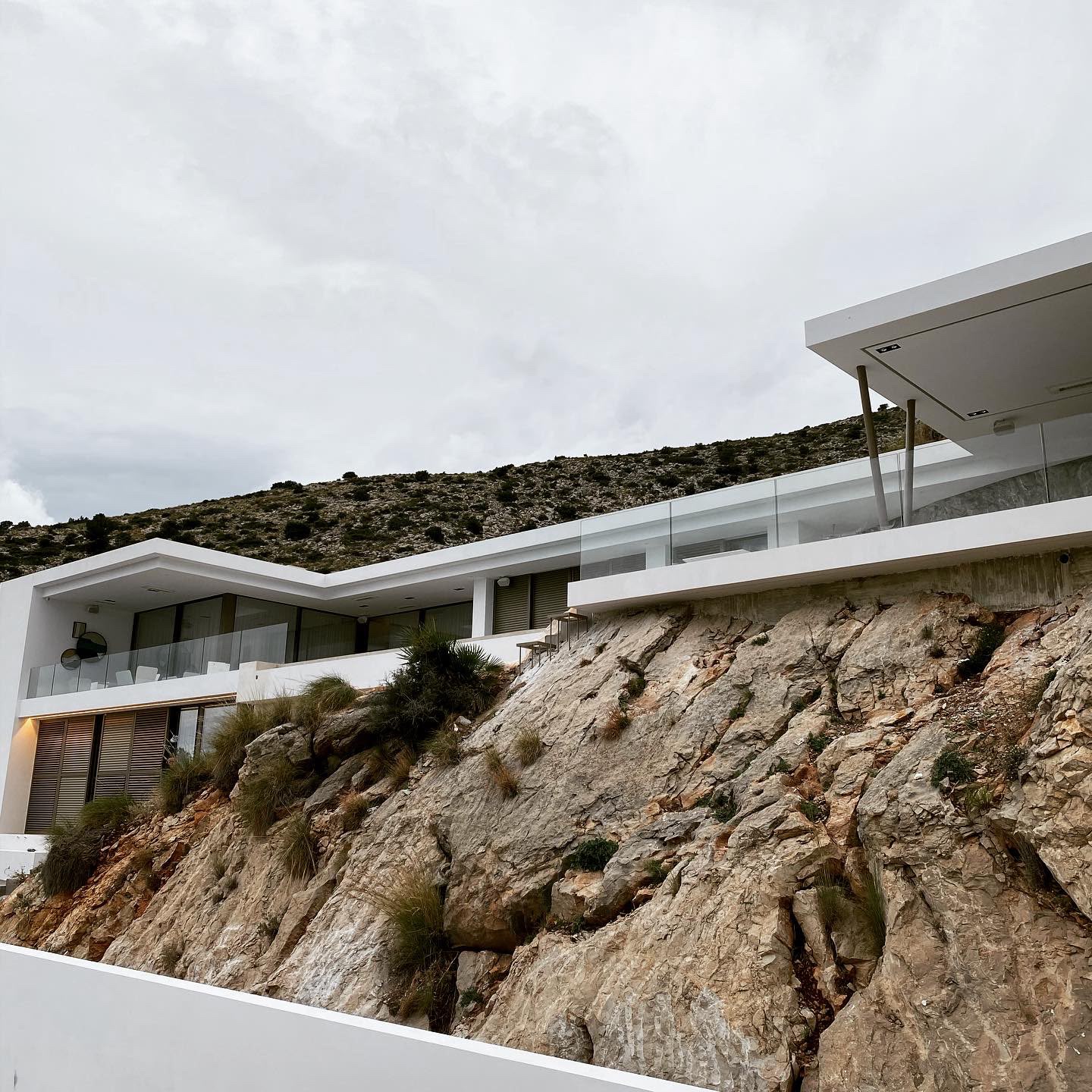 Hvit villa med utkragede tak og glassrekkverk bygget rett i fjellsiden