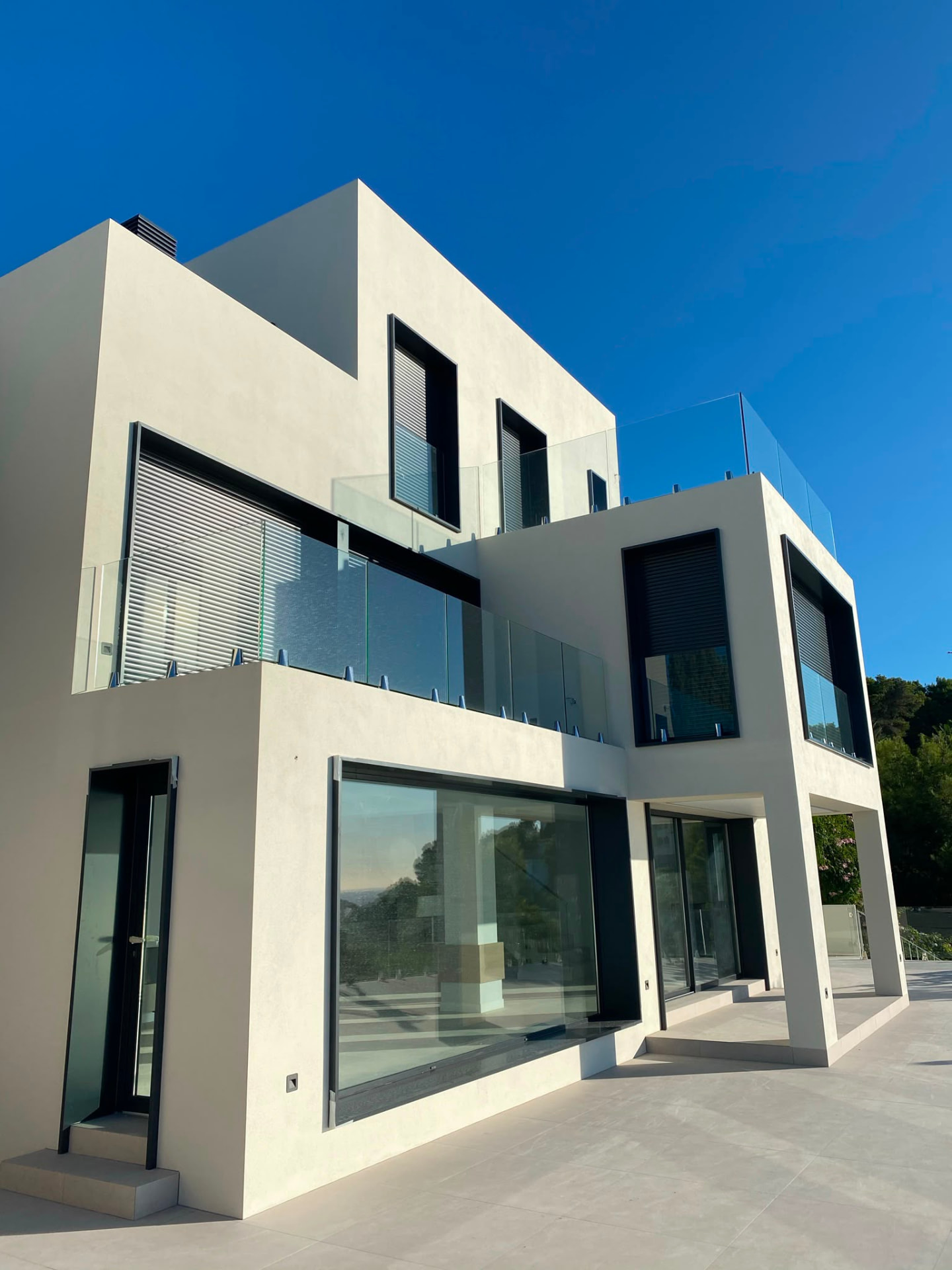 Hvit villa i to etasjer med glassrekkverk mot klar blå himmel