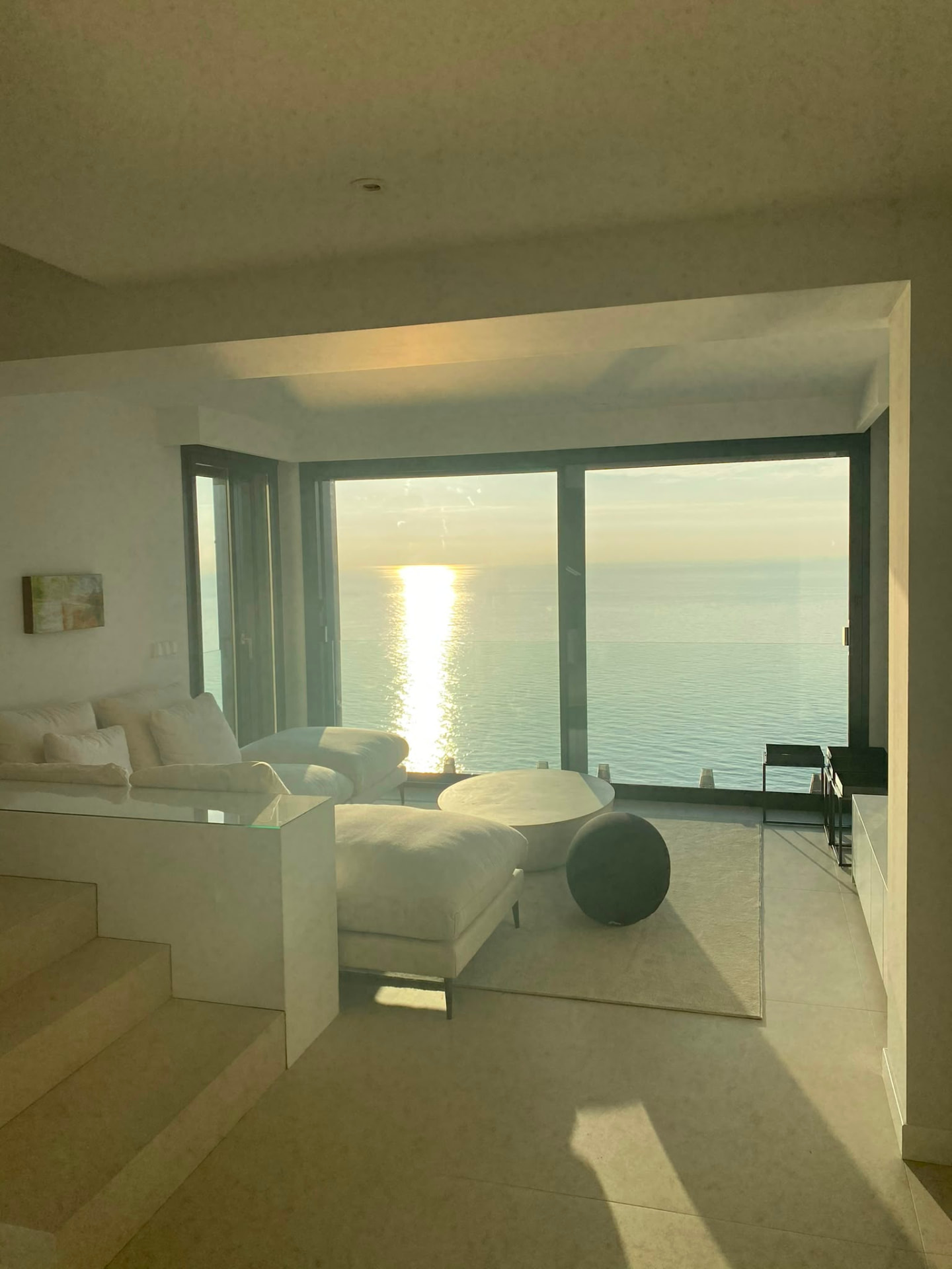 Stue med store skyvedører i glass og solnedgang over havet